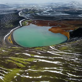 An aqua blue lagoon sits in the middle of the valley of Landmannalaugar, Iceland