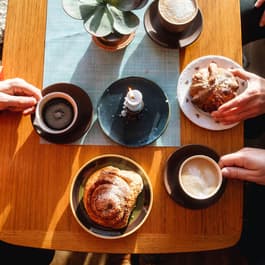 A top down photo of a group of friends holding coffee and pastries at a sunlit table in the Lofoten Islands