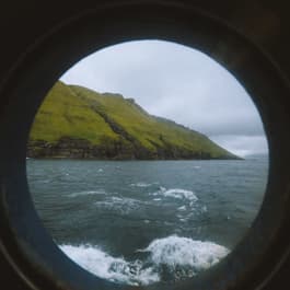 Looking through the porthole of a ferry boat out onto the green coast of the Faroe Islands