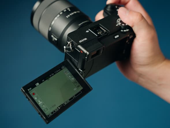 The Sony A6700 Review & Walkthrough — Image of a hand holding the camera against a blue background.