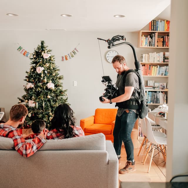 Evan with a camera rig in a home living room filming a family sitting on a couch