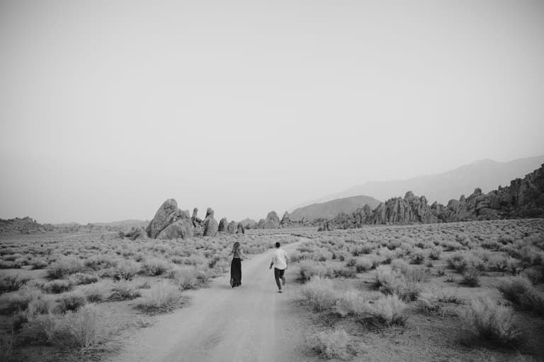 Black and white frame of two people walking in the distance in a desert location.