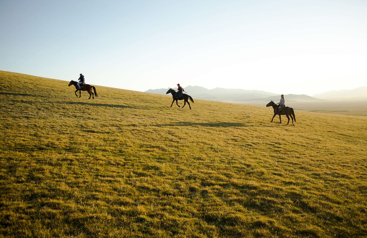 Three people horseback riding up to the Song Kul Panoramic Viewpoint in Kyrgyzstan