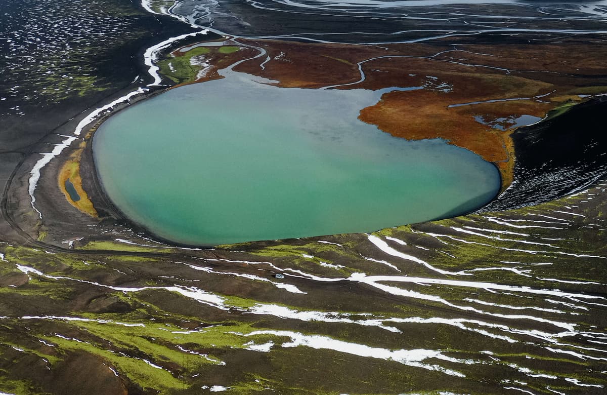 An aqua blue lagoon sits in the middle of the valley of Landmannalaugar, Iceland