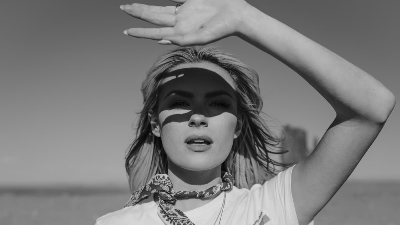 Black and white portrait of a woman holding her hand out to shield the sun from her eyes.