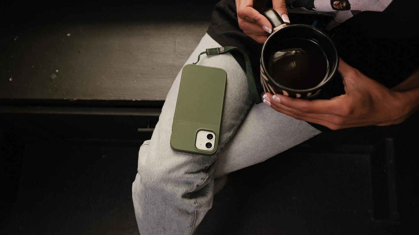 Person sitting with a cup of coffee with their iPhone 12 with Moment case and wrist strap resting on their lap.