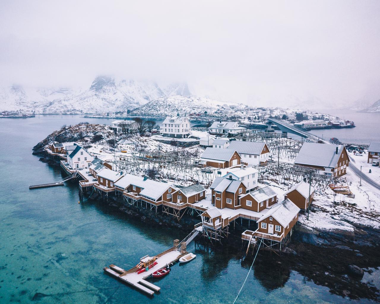 A small coastal town in the snowy winter season with foggy mountains in the background.