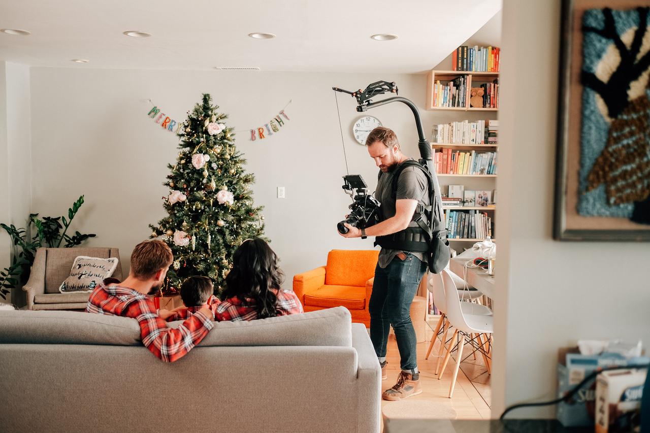 Evan with a camera rig in a home living room filming a family sitting on a couch