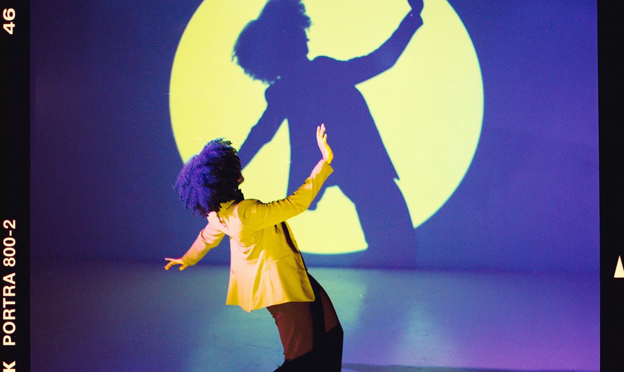 Film photo of woman and her silhouette in a yellow spotlight with purple background