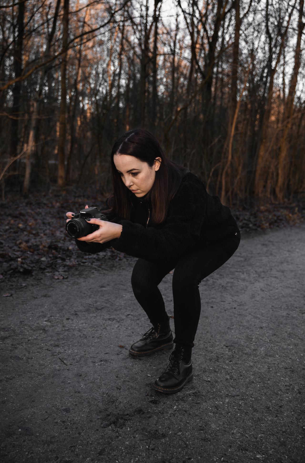 Lila crouching on a wooded path holding a camera