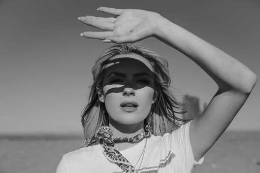 Black and white portrait of a woman holding her hand out to shield the sun from her eyes.