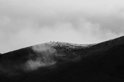 Black and white frame of a few people out in the distance walking through rolling hills.