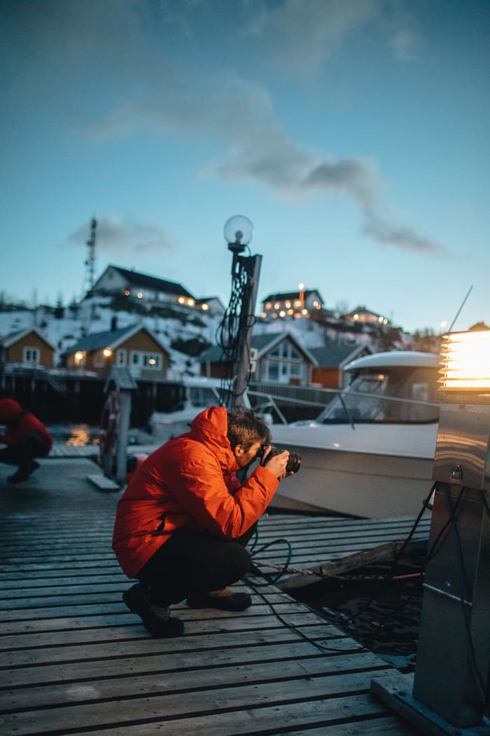 Max Chesnut crouches on a boat dock in the Lofoten Islands, taking photos during blue hour