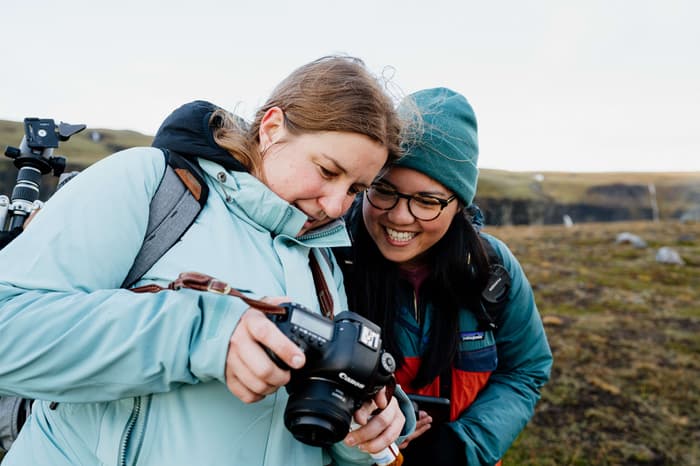 Two girls in blue jackets smile as they look at a photo on a camera in Iceland