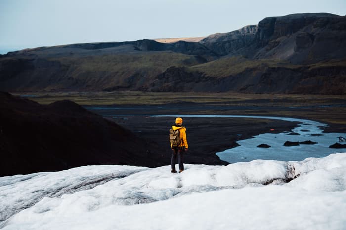 A man in a yellow jacket helmet stands on Solheimajokull Glacier in Iceland