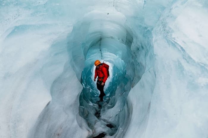 A man in a red jacket climbs through a glacier in Solheimajokull Iceland
