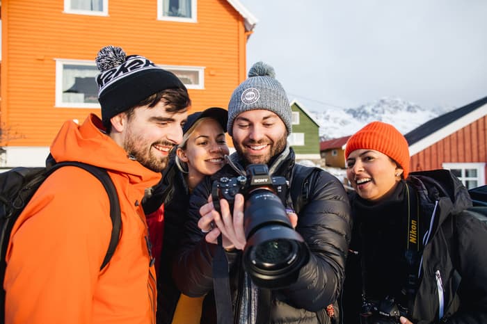 A group of friends look at a photo on a camera in front of the Lofoten Island's colorful cabins