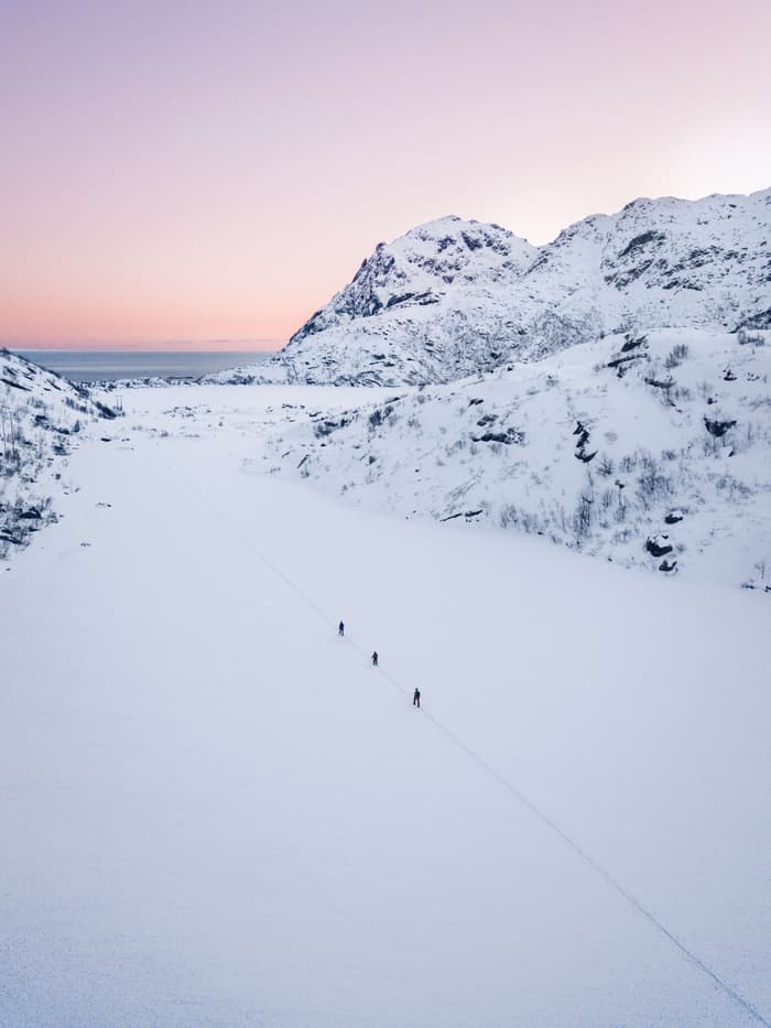 Three hikers ascend Stuvdalsvatnet at sunrise as the sky begins to glow pink and purple